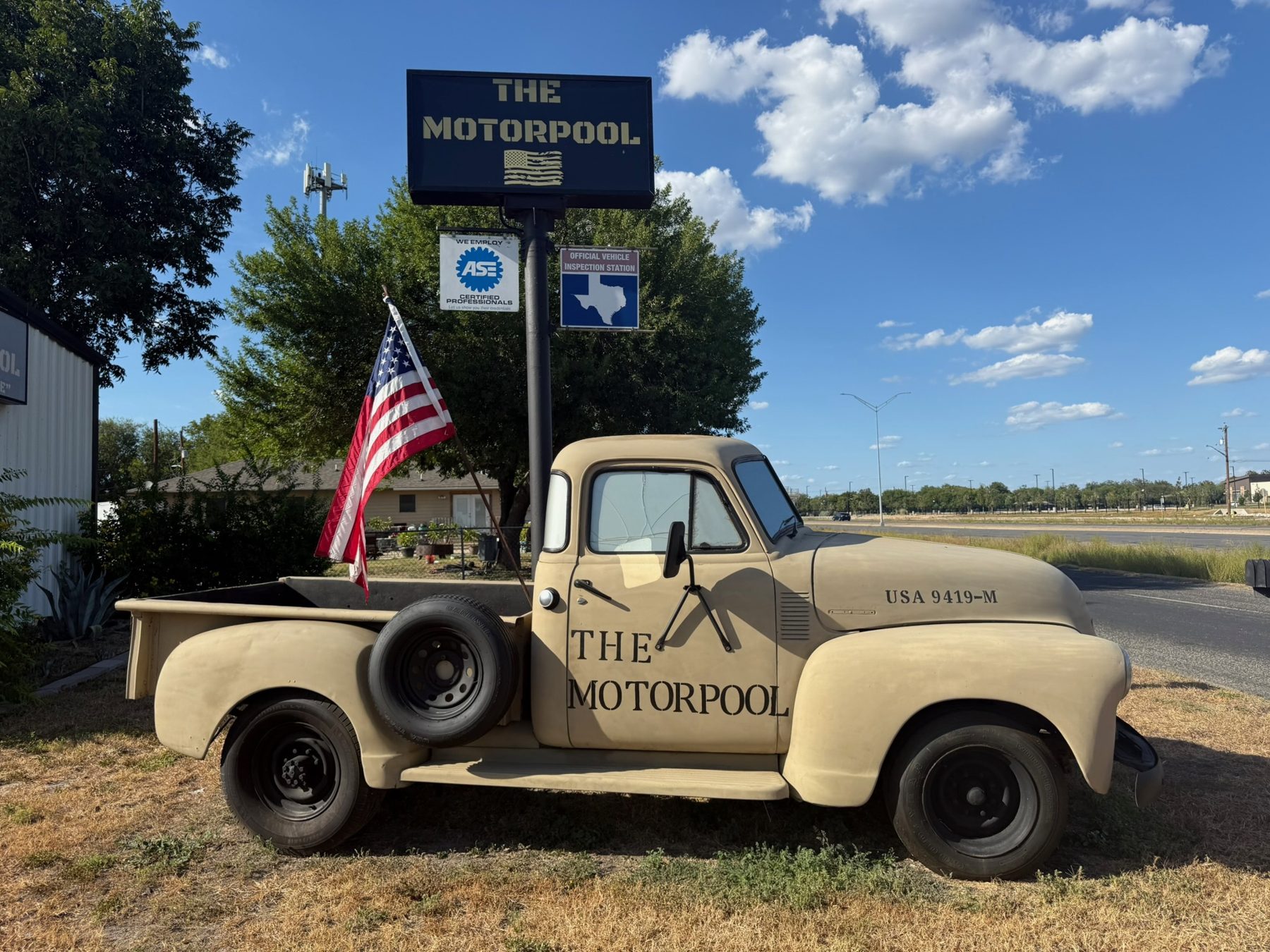 The Motorpool's vintage tan truck parked under the shop sign with an American flag